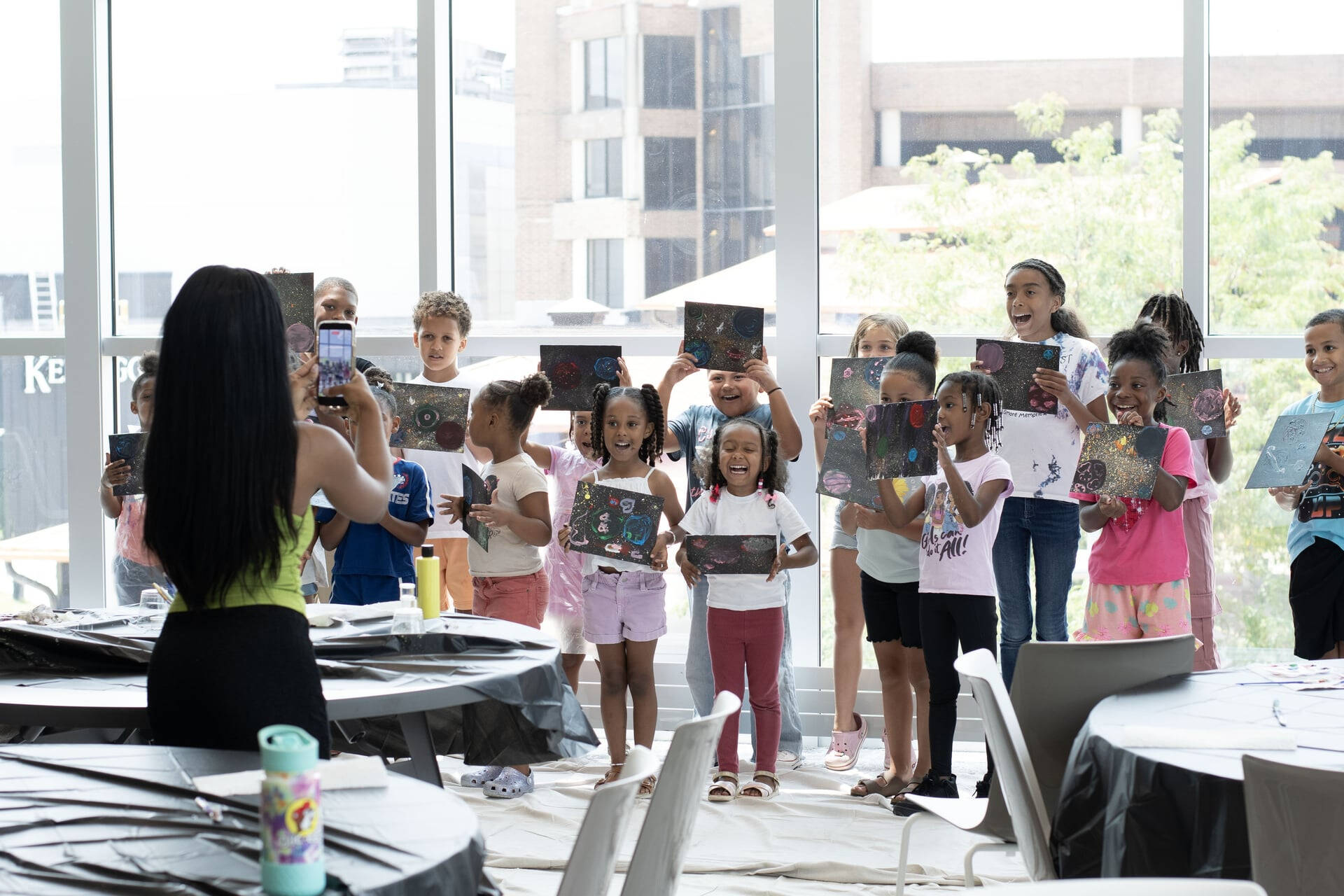 Jamari Taylor takes a cell phone photo of young artists holding up their artwork in the Battle Creek Innovation Hub